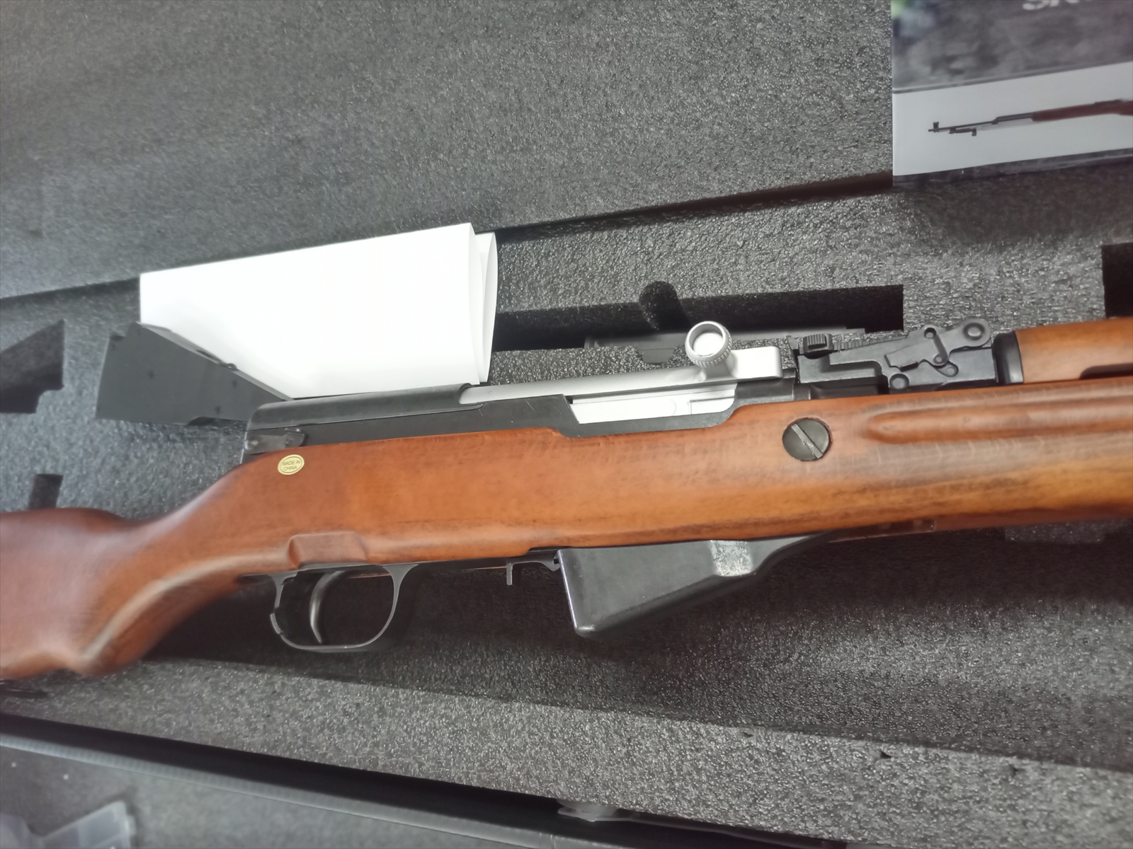 Bolt-action rifle with a wooden stock resting in a foam-padded case, exposed bolt and trigger area visible